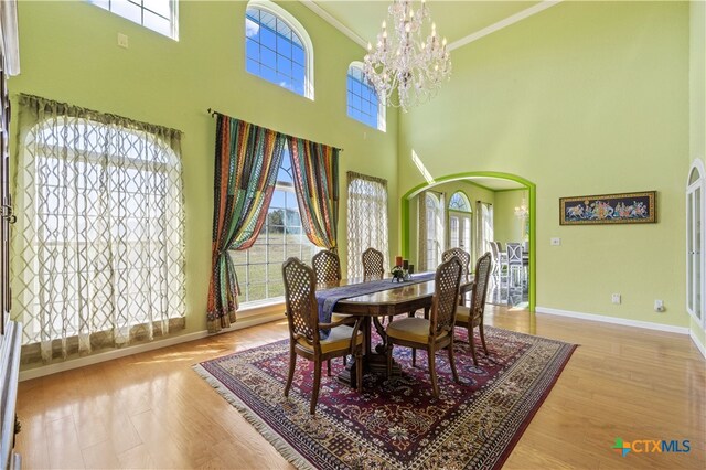 dining space featuring a towering ceiling, wood-type flooring, crown molding, and plenty of natural light