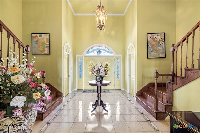 tiled entrance foyer featuring crown molding, a high ceiling, and an inviting chandelier