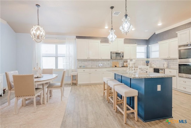 kitchen with white cabinetry, hanging light fixtures, stainless steel appliances, a center island, and light stone countertops