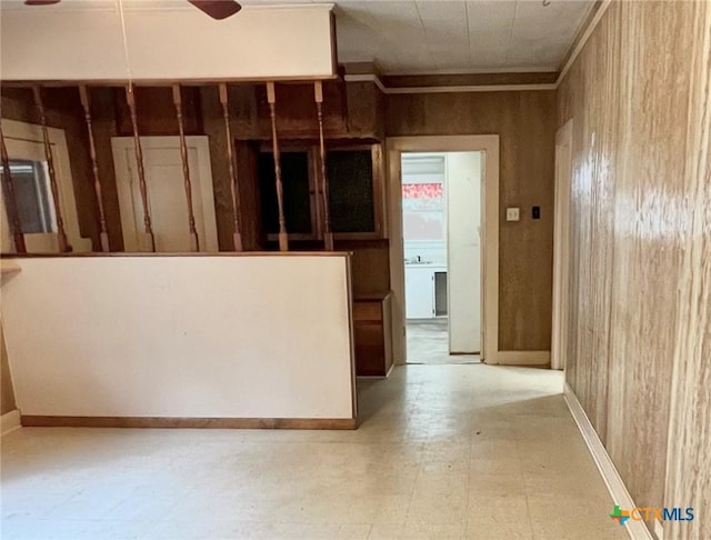 interior space featuring tile patterned floors, ornamental molding, ceiling fan, baseboards, and wooden walls