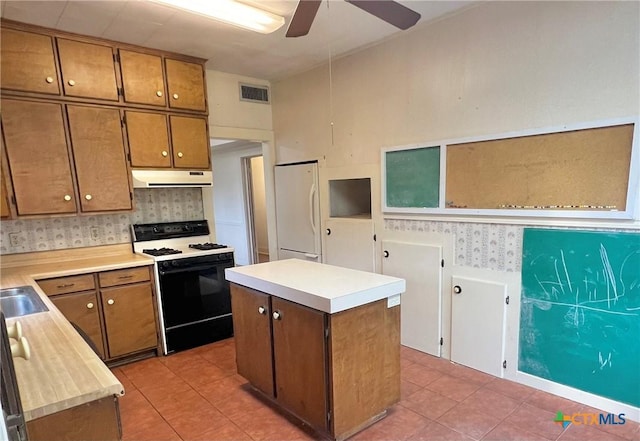 kitchen with under cabinet range hood, a ceiling fan, gas stove, wallpapered walls, and freestanding refrigerator