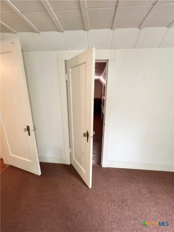 unfurnished room featuring dark carpet and baseboards