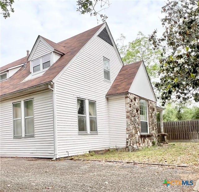 view of property exterior featuring stone siding, fence, and roof with shingles