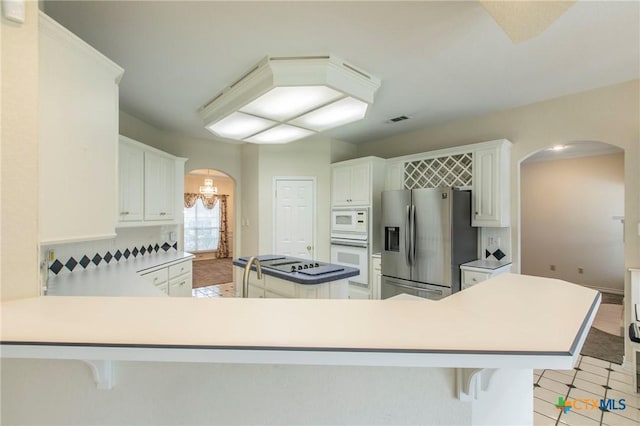 kitchen featuring a kitchen breakfast bar, white appliances, white cabinetry, and kitchen peninsula