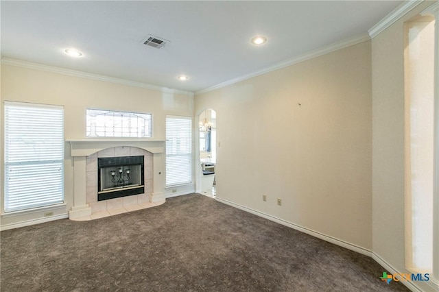 unfurnished living room featuring a tiled fireplace, ornamental molding, carpet, and plenty of natural light