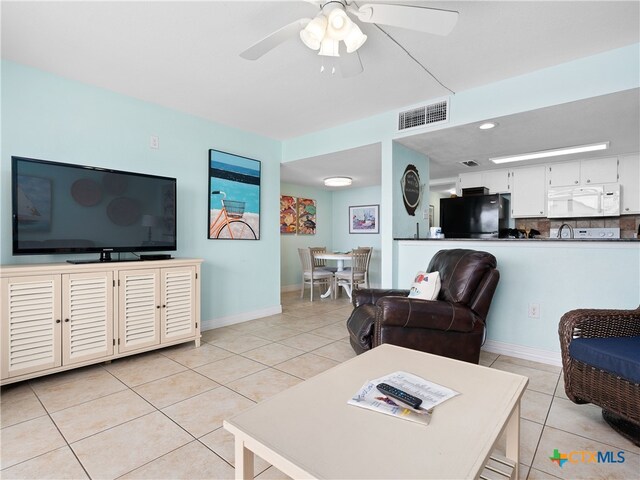 living area with light tile patterned floors, ceiling fan, and baseboards