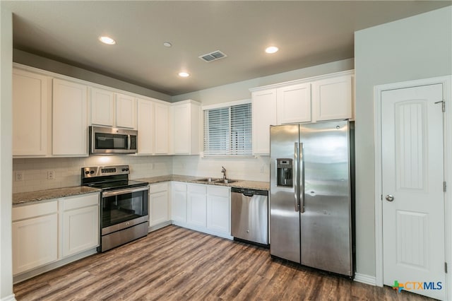 kitchen with stainless steel appliances, light stone countertops, white cabinets, and dark wood-type flooring