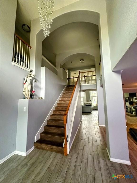 stairway with a towering ceiling, hardwood / wood-style floors, and an inviting chandelier