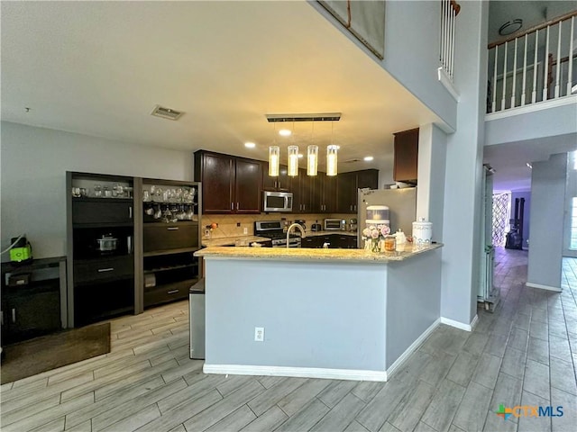 kitchen with pendant lighting, kitchen peninsula, stainless steel appliances, light stone countertops, and dark brown cabinets