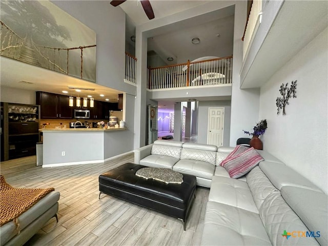 living room with a towering ceiling, ceiling fan, and light hardwood / wood-style flooring