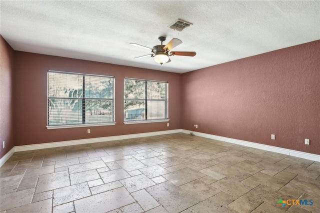 unfurnished room featuring stone tile floors, a textured wall, visible vents, a textured ceiling, and ceiling fan