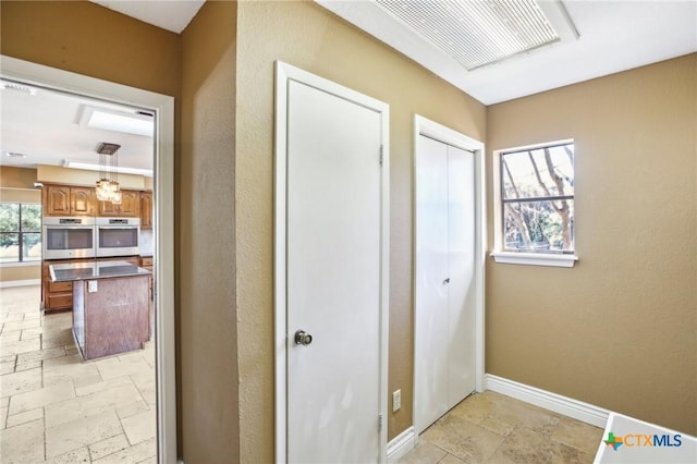 hallway with stone tile flooring, visible vents, and baseboards