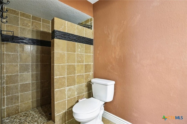 full bathroom featuring a tile shower, toilet, and a textured wall