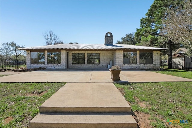 ranch-style home featuring a chimney, brick siding, a patio area, and metal roof