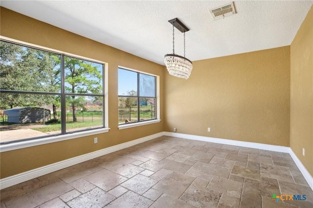 empty room featuring stone tile floors, baseboards, visible vents, and an inviting chandelier