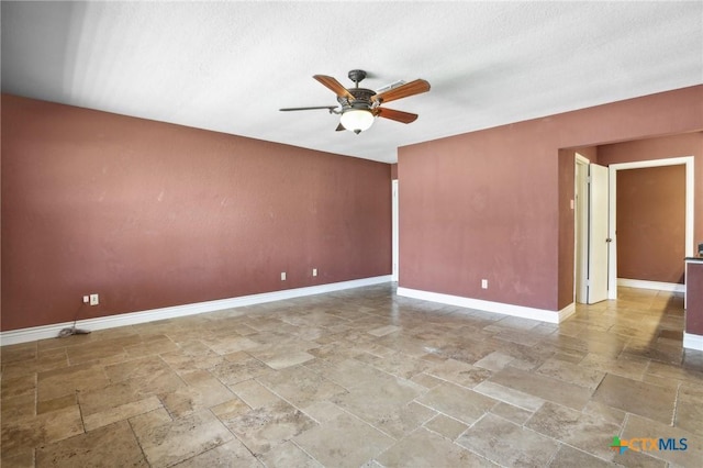 unfurnished room with stone tile floors, a ceiling fan, and baseboards