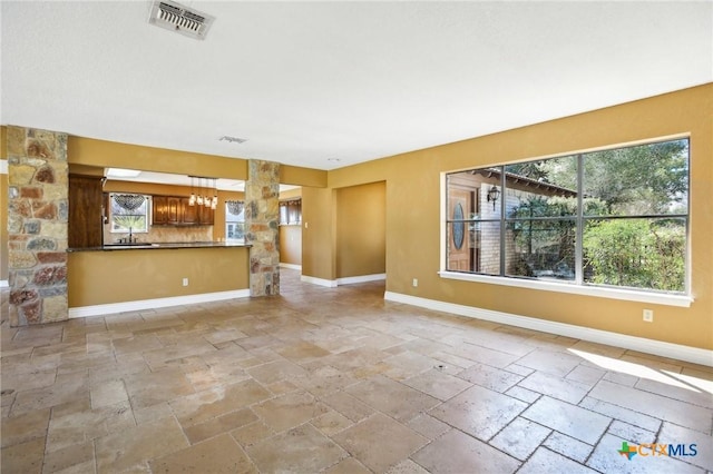 unfurnished living room featuring baseboards, stone tile flooring, visible vents, and plenty of natural light