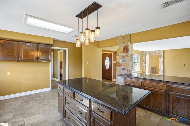 kitchen featuring dark stone counters, a center island, stone tile flooring, baseboards, and visible vents