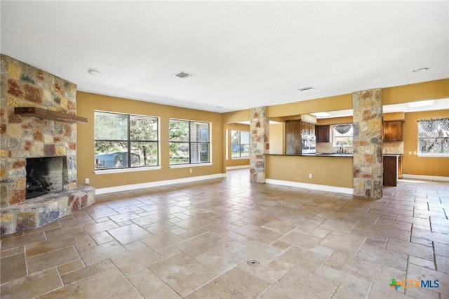 unfurnished living room featuring plenty of natural light, baseboards, visible vents, and a stone fireplace