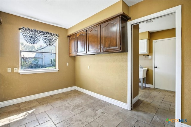 laundry area with baseboards and stone tile flooring