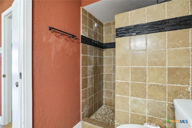 bathroom featuring a tile shower, a textured wall, and toilet