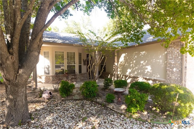 view of front of home with a patio area, a shingled roof, stucco siding, and brick siding