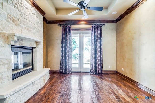 unfurnished living room with a raised ceiling, a stone fireplace, crown molding, and dark hardwood / wood-style floors