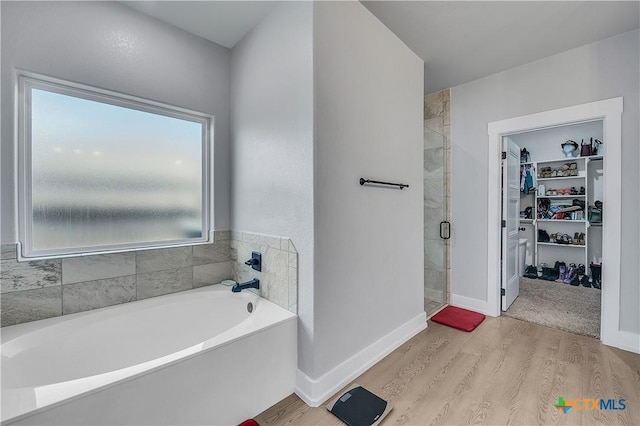 bathroom featuring a walk in closet, a shower stall, a bath, and wood finished floors