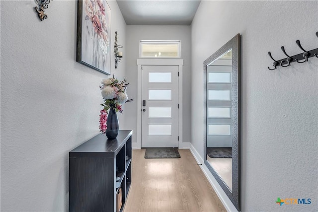 doorway with light wood-style floors, a textured wall, and baseboards