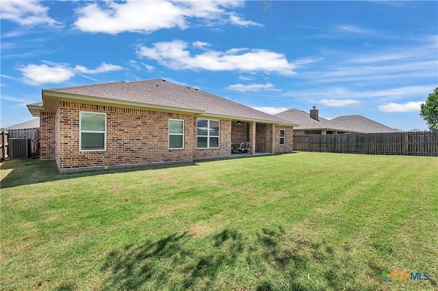 rear view of property featuring brick siding, a yard, and a fenced backyard