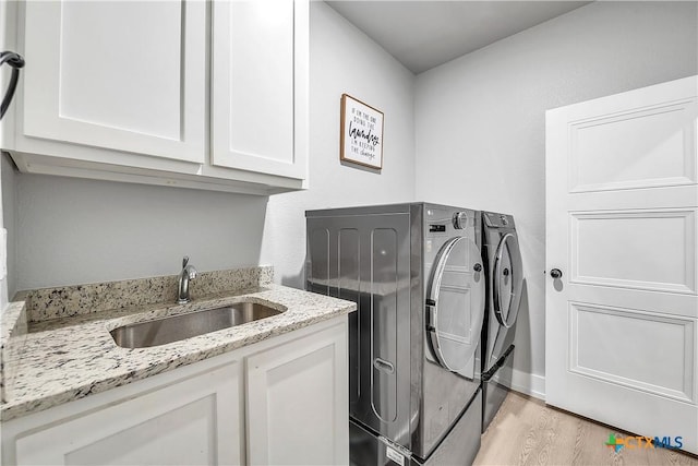 laundry area featuring washer and dryer, cabinet space, a sink, and light wood-style flooring