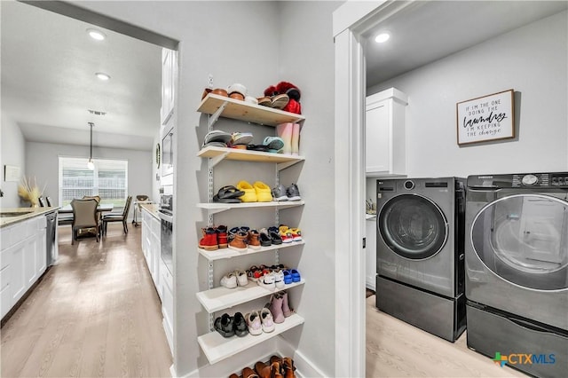 laundry room with light wood finished floors, cabinet space, washer and clothes dryer, and a sink