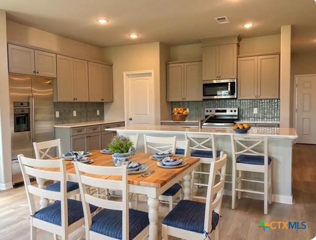 837 Swallow Dr, Palacios, TX 77465 - kitchen with stainless steel appliances, light countertops, light wood-style floors, gray cabinetry, and tasteful backsplash