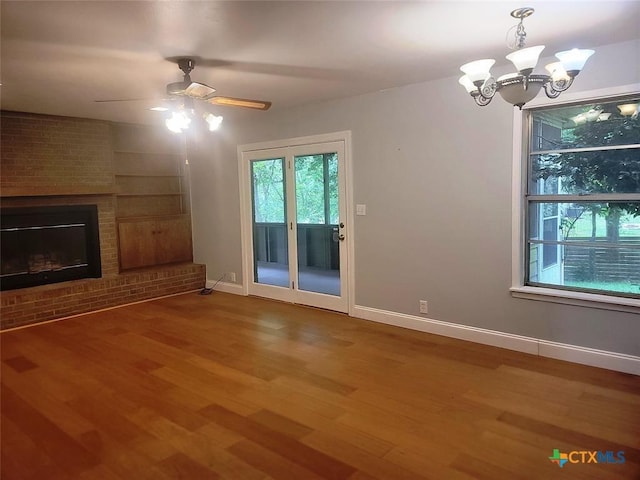 unfurnished living room featuring ceiling fan with notable chandelier, wood-type flooring, and a fireplace