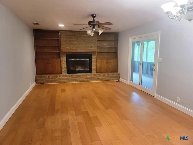 unfurnished living room featuring built in shelves, ceiling fan, light wood-type flooring, and a brick fireplace