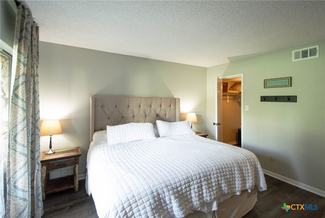 bedroom with dark hardwood / wood-style floors, a textured ceiling, a closet, and a walk in closet