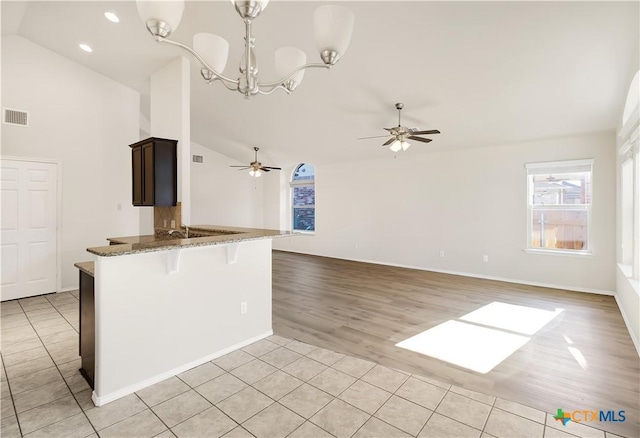 kitchen with light tile patterned floors, ceiling fan with notable chandelier, vaulted ceiling, and stone counters