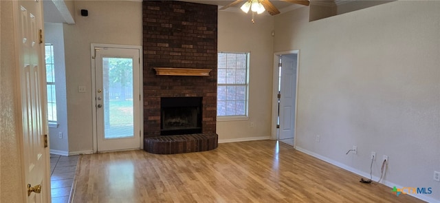 unfurnished living room featuring ceiling fan, a towering ceiling, light hardwood / wood-style floors, and a fireplace