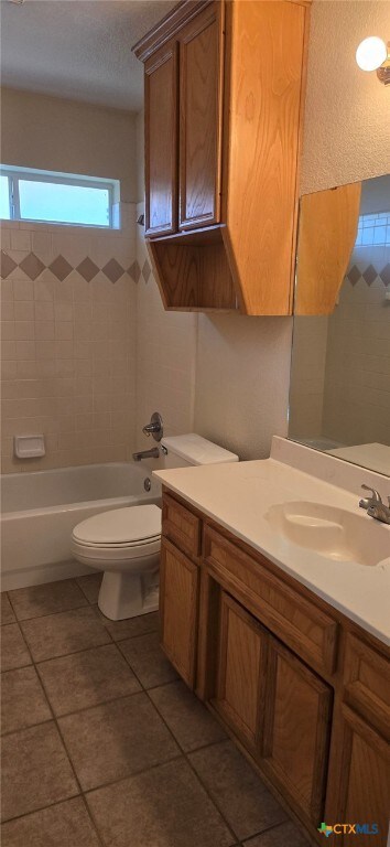 full bathroom featuring toilet, tiled shower / bath combo, vanity, and tile patterned floors