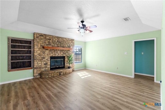 unfurnished living room with baseboards, visible vents, a ceiling fan, wood finished floors, and a brick fireplace