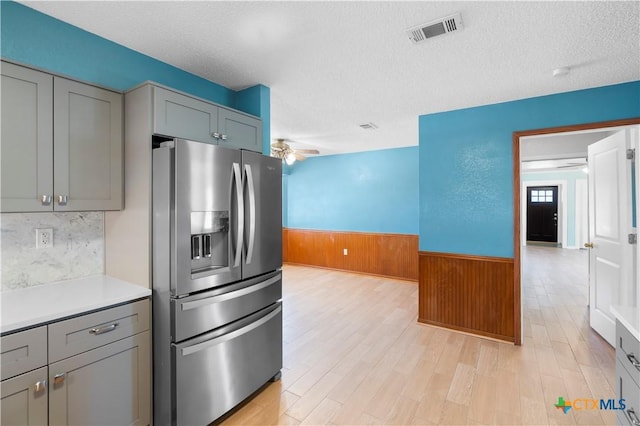 kitchen featuring a textured ceiling, a wainscoted wall, visible vents, gray cabinets, and stainless steel fridge