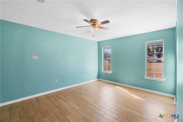 empty room with a textured ceiling, wood finished floors, a ceiling fan, and baseboards