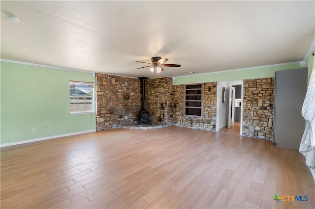 unfurnished living room featuring a ceiling fan, a wood stove, crown molding, and wood finished floors