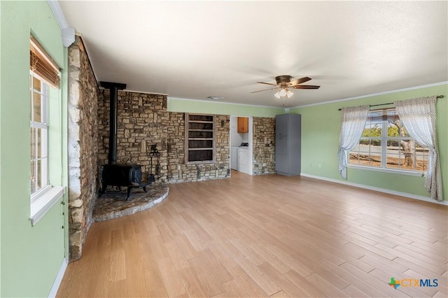 unfurnished living room featuring crown molding, a ceiling fan, a wood stove, and light wood-style floors