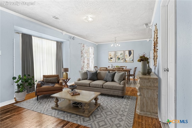 living room featuring ornamental molding, wood-type flooring, a chandelier, and a textured ceiling