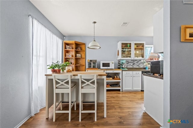 kitchen with visible vents, open shelves, white microwave, and light wood-style flooring