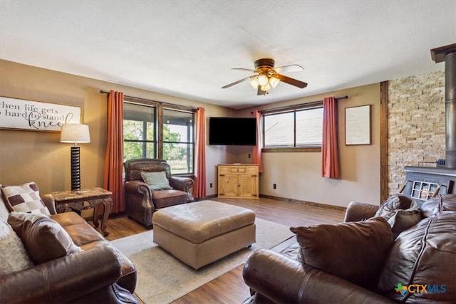 living room featuring a wood stove, ceiling fan, and light hardwood / wood-style flooring