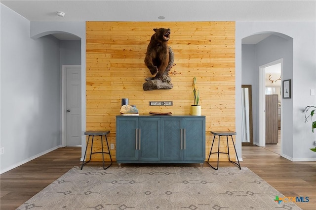 bar with baseboards, arched walkways, wooden walls, and wood finished floors