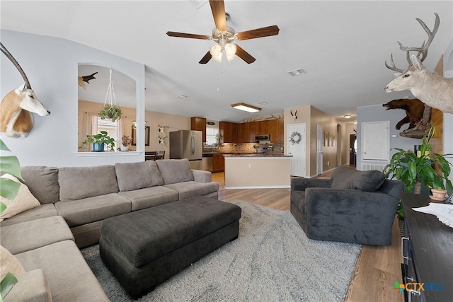 living room featuring light wood finished floors, visible vents, a ceiling fan, and vaulted ceiling