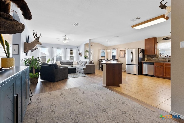 kitchen featuring a healthy amount of sunlight, visible vents, lofted ceiling, appliances with stainless steel finishes, and brown cabinets